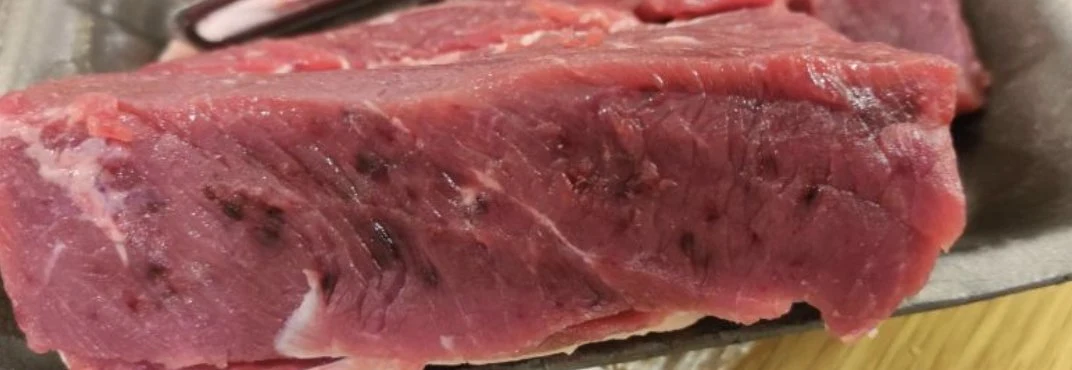 Meat with pronounced dark discoloration under the surface, illustrating bleeding in muscle tissue